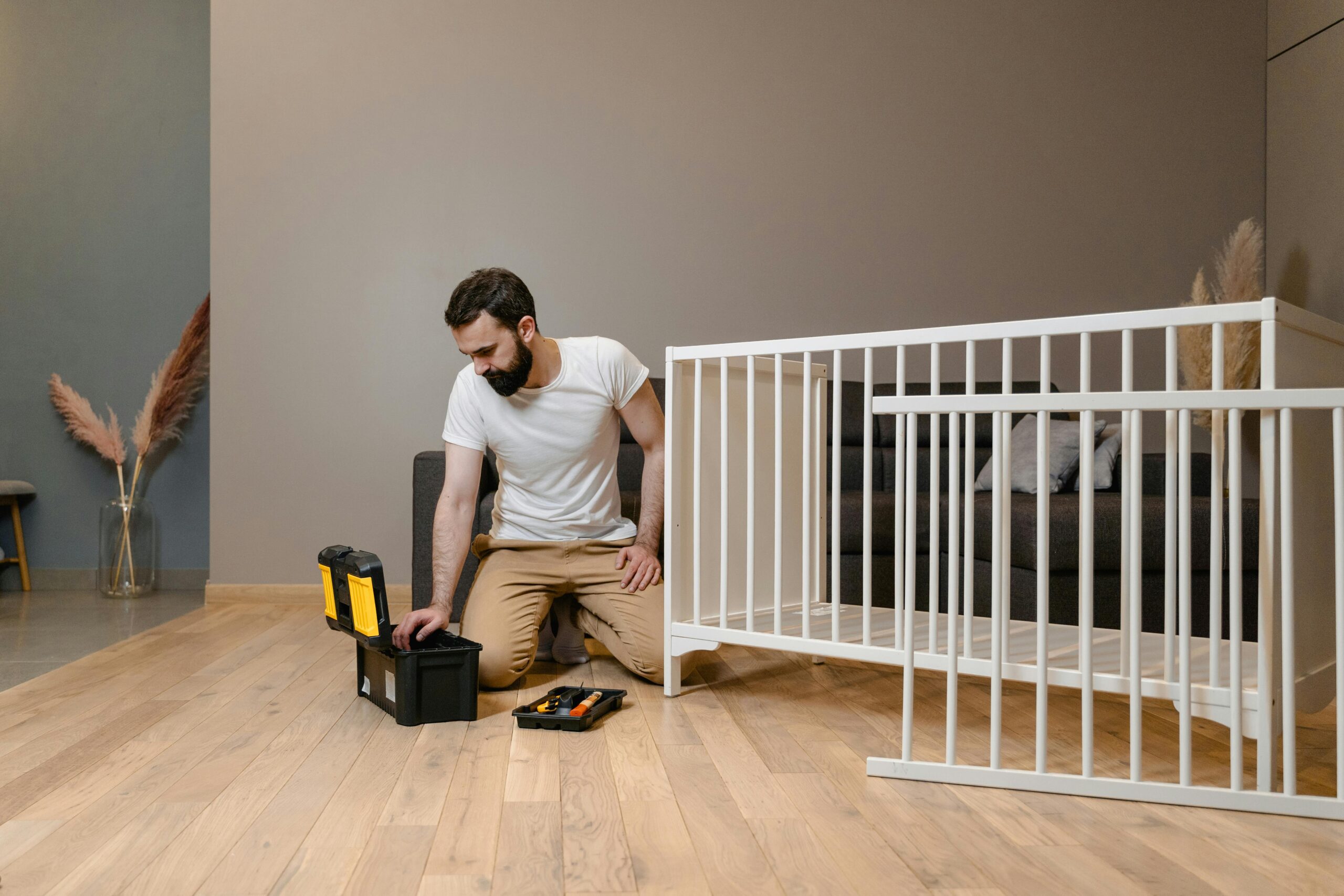 A man assembling a white crib indoors with tools, focusing on DIY and home care.